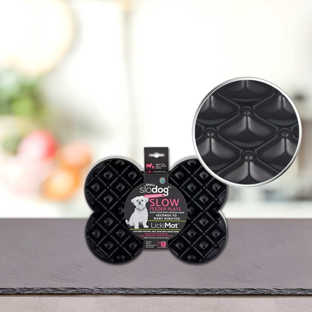 PLATINUM Podloga LickiMat® - SLODOG, črna podloga v obliki kosti za pse s počasnim hranjenjem, ima teksturirano dvignjeno geometrijsko površino. Prikazano v embalaži s povečanim delom, ki poudarja podrobnosti hranilnika; zamegljeno ozadje.