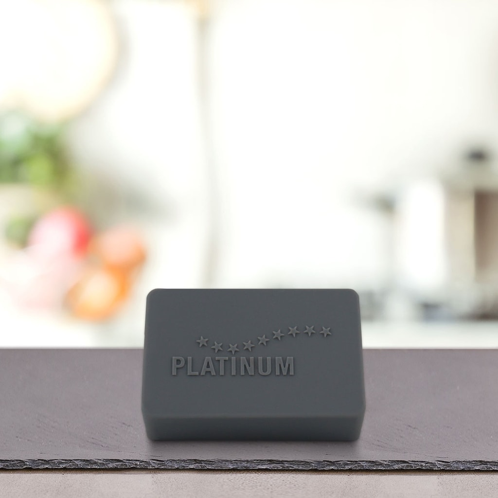 Temna pravokotna ploščica z napisom PLATINUM Praktičen Pokrovček MENU za shranjevanje Mokre Hrane, ki jo krasi krivulja zvezd, stoji na gladki površini na zamegljenem kuhinjskem ozadju.