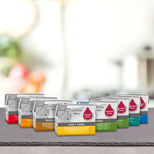 Na mizi je postavljenih več škatel mačje hrane v pisani embalaži. V svetlem notranjem ozadju lahko opazite PLATINUM Poskusni paket Mini: Najboljše izbira za pse manjših pasem, kot nalašč za pse majhnih pasem.