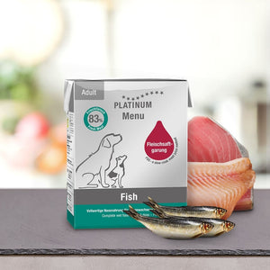 Škatla PLATINUM Poskusni paket različnih okusov Mokre Hrane za Pse stoji na pultu v bližini svežih ribjih filejev, na embalaži so ilustracije psov in informacije o izdelku, ki poudarjajo kakovostna pasja hrana s svežim mesom.