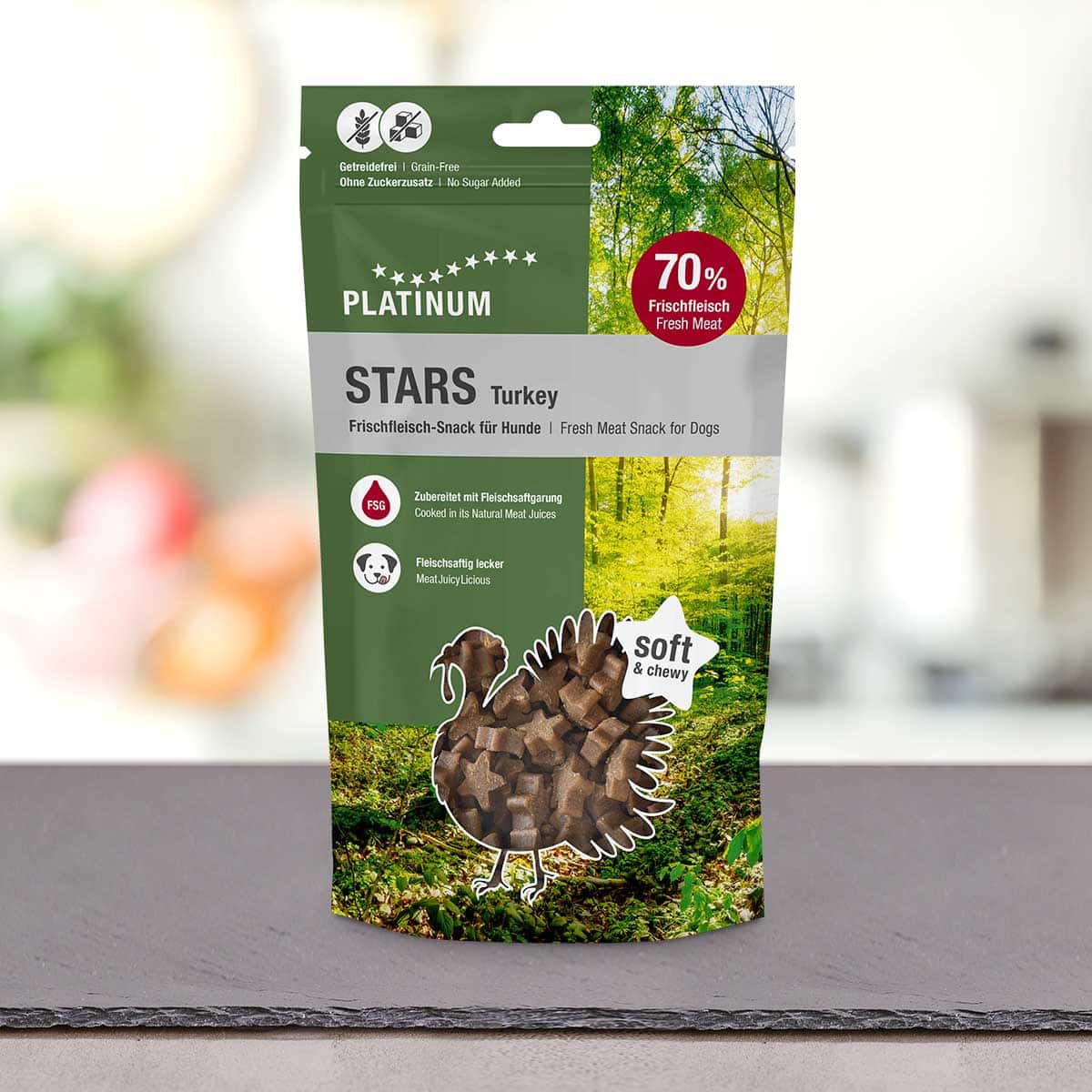Stoječa vrečka PLATINUM Stars Turkey 185g - najboljša nagrada iz 100 % svežega puranjega mesa za pse je prikazana na leseni površini z gozdnim motivom, ki poudarja mehke in žvečljive prigrizke ter vrhunsko puranje meso.