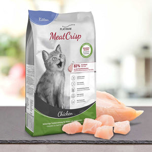 Vrečka PLATINUM MeatCrisp Kitten Chicken, Suha Hrana za Mačke stoji ob surovem piščancu na pultu. Na embalaži je prikazan siv maček, podatki o hranilni vrednosti in omenjen poseben postopek Freshmeatdryer.